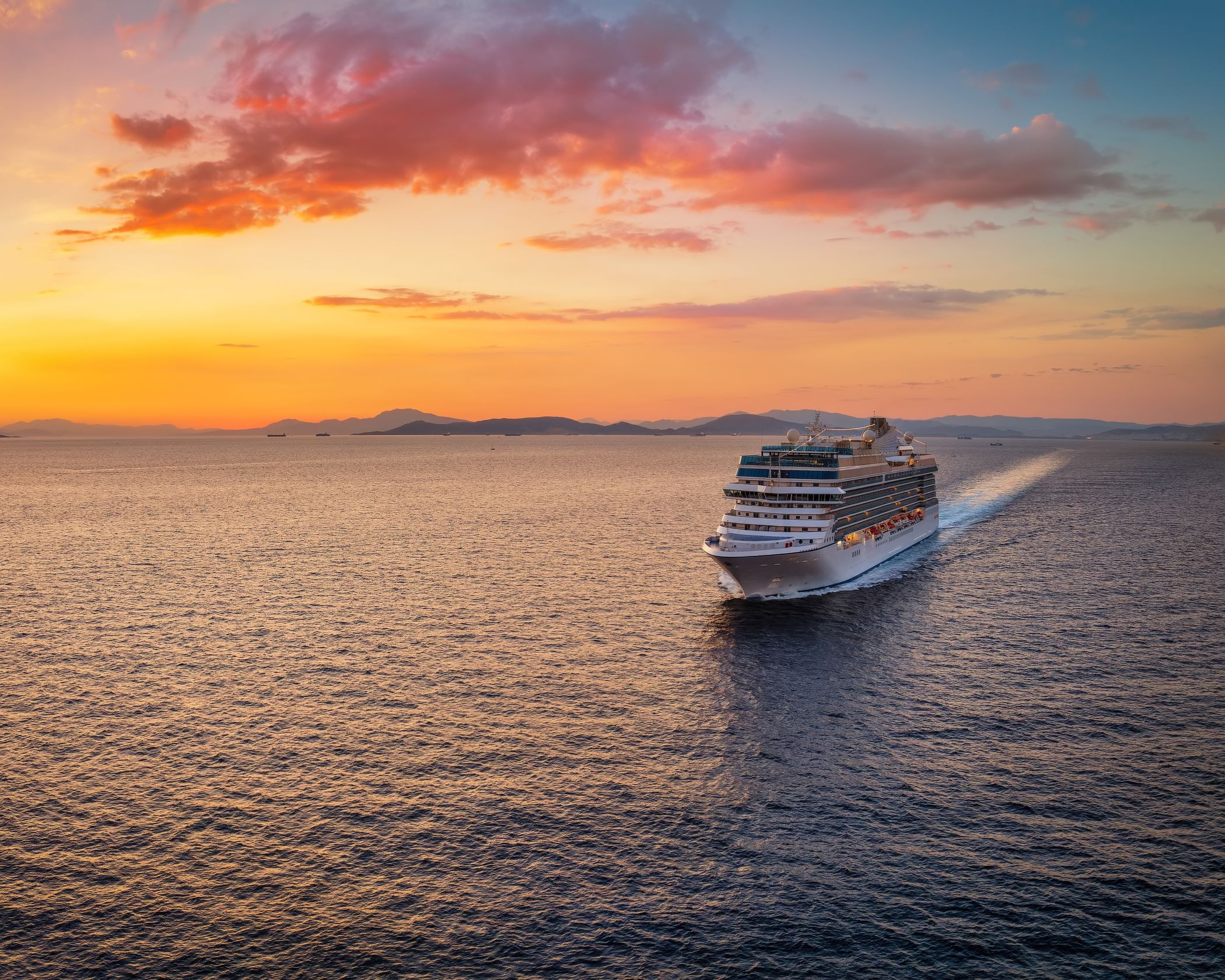 Luftaufnahme eines Kreuzfahrtschiffs, das bei goldener Abendsonne über das Meer fährt | © Adobe Stock