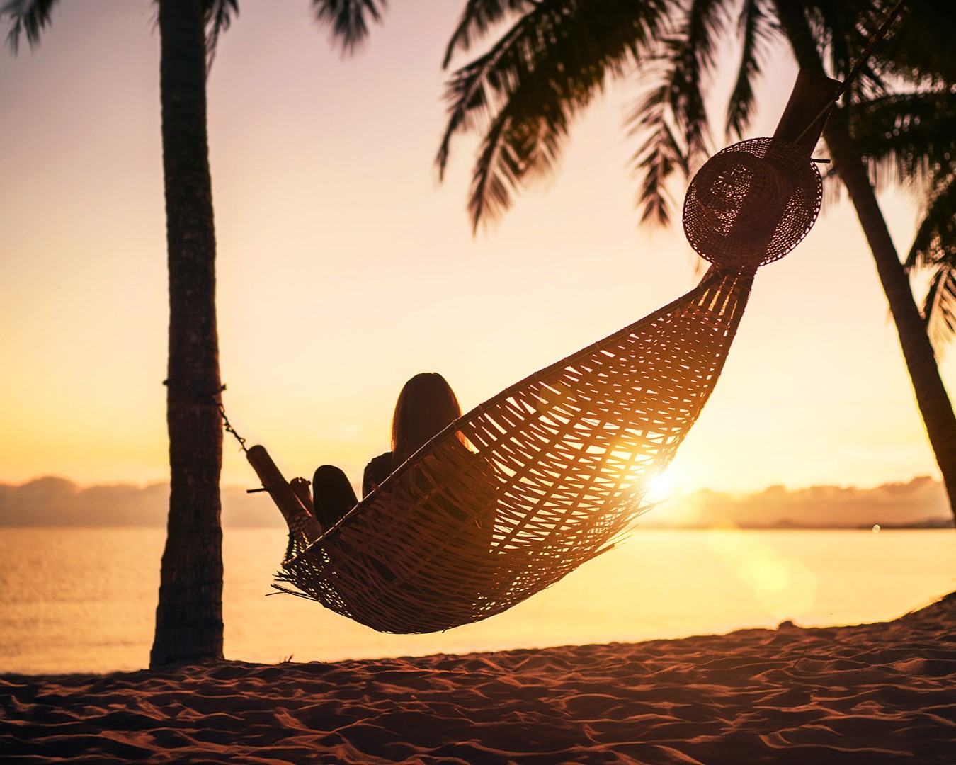 Frau entspannt in der Hängematte zwischen Palmen am Strand im Sonnenuntergang | © Adobe Stock