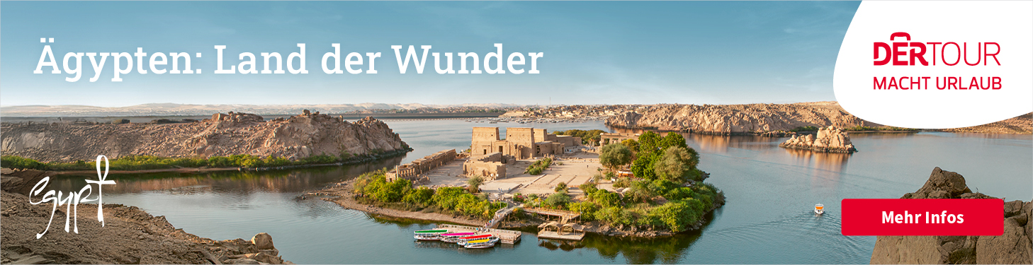 Luftaufnahme einer kleinen Insel im Nil mit alten ägyptischen Tempelruinen, umgeben von ruhigem Wasser. Mehrere bunte Boote liegen am Ufer, im Hintergrund sieht man felsige Uferlandschaften und die weitläufige Flusslandschaft. | © DERTOUR