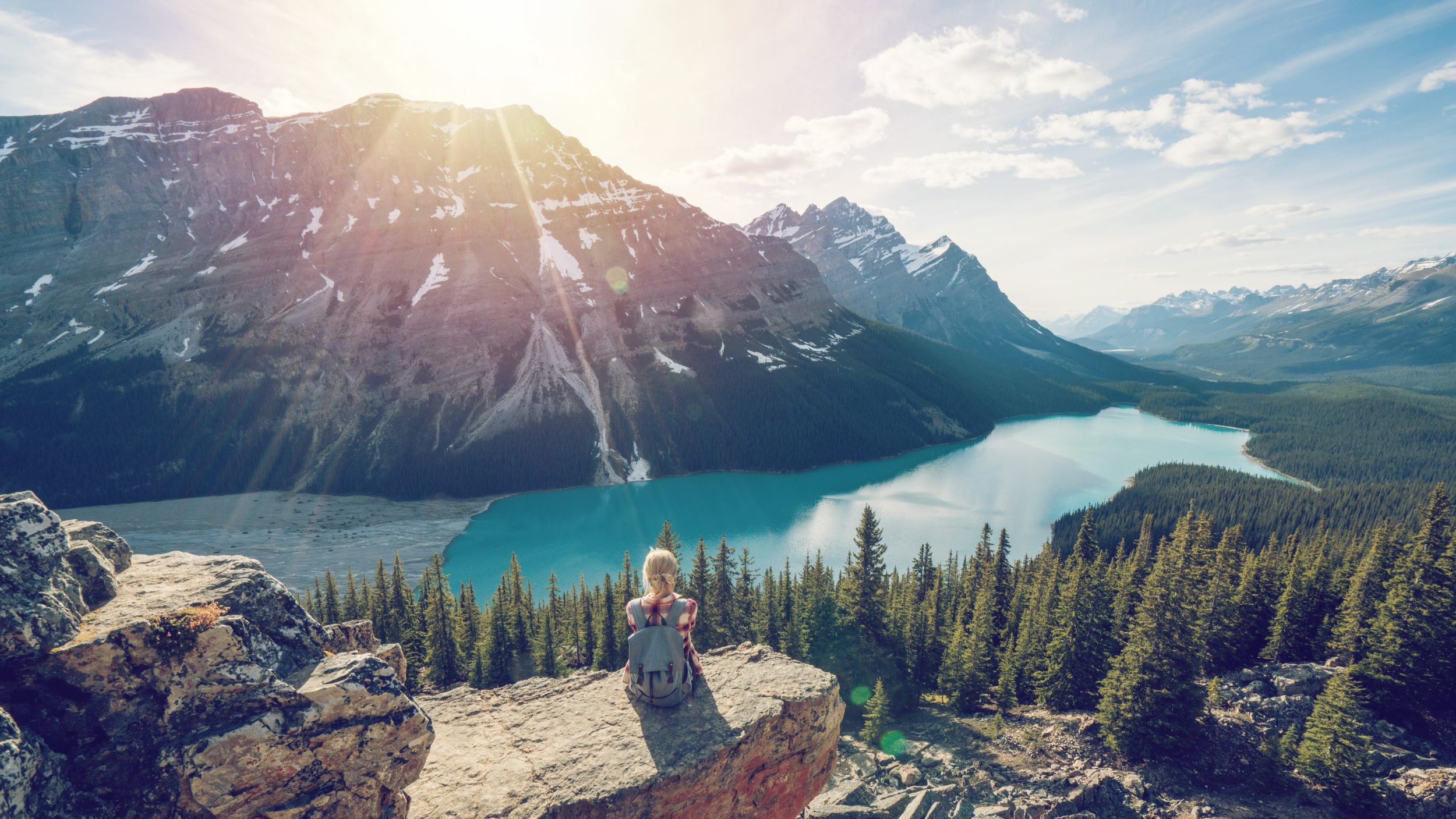 Junge Wanderin sitzt auf einem Felsen über einem Bergsee im Frühling und blickt in die Ferne | © Berge & Meer/Getty Images